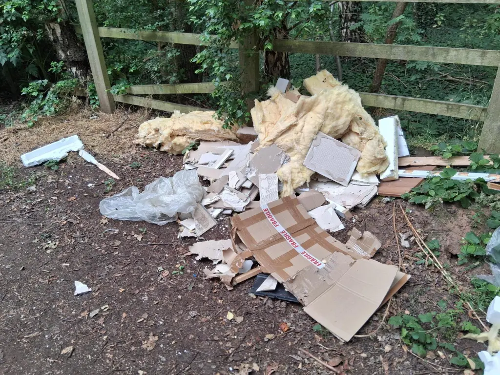 Insulation, plasterboard and cardboard dumped beside a fence at the edge of woodland