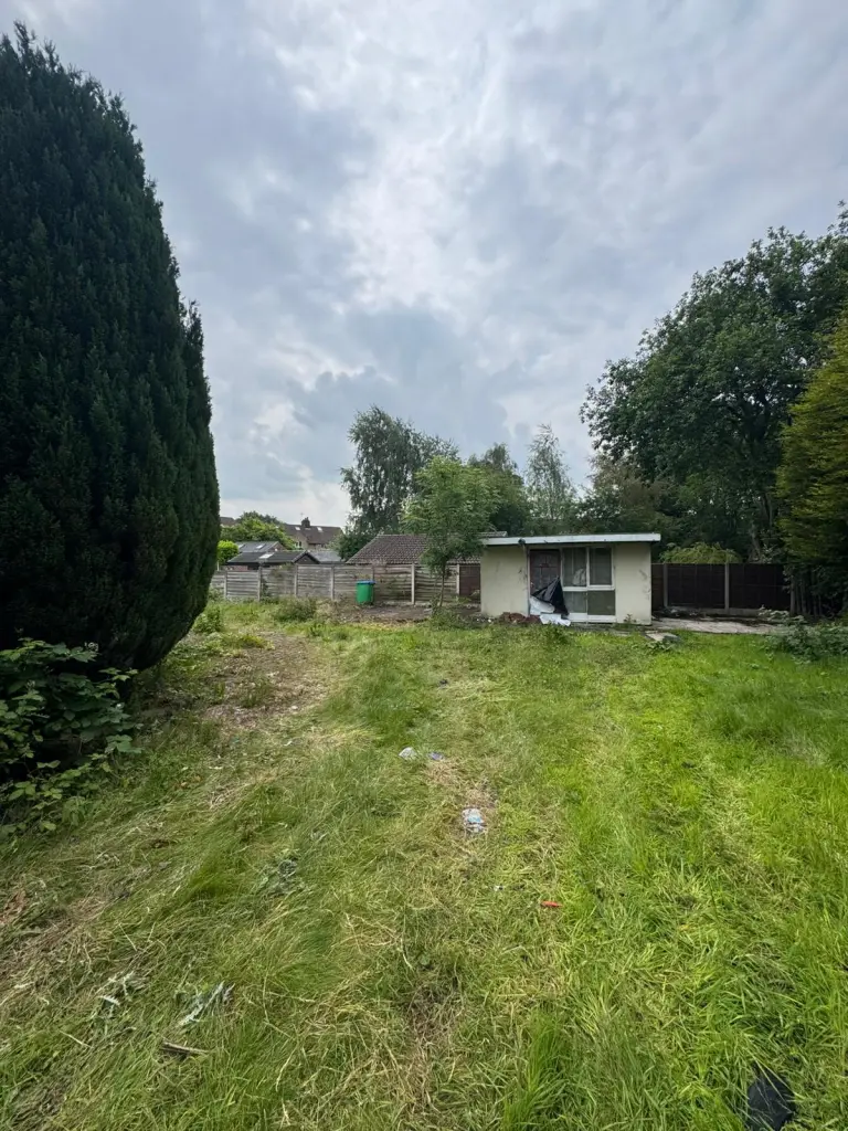 Cleared lawn leading to a small outbuilding, lined by trees