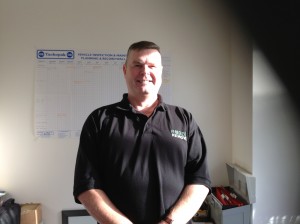 Smiling man in a black Rubbish Removers polo shirt standing in an office