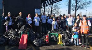 Volunteers in matching T-shirts standing behind a large pile of full black litter-pick bags