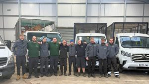 Uniformed team lined up in front of white caged tipper trucks inside a depot