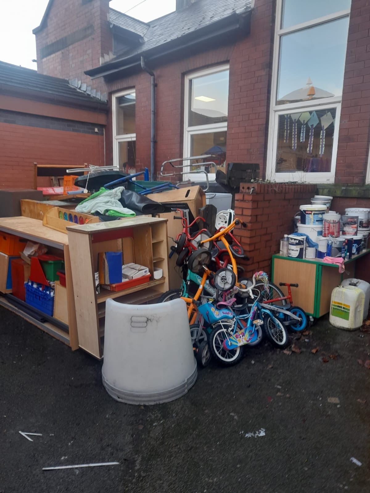 Furniture, children's bikes, a bin and household items gathered outside a brick building
