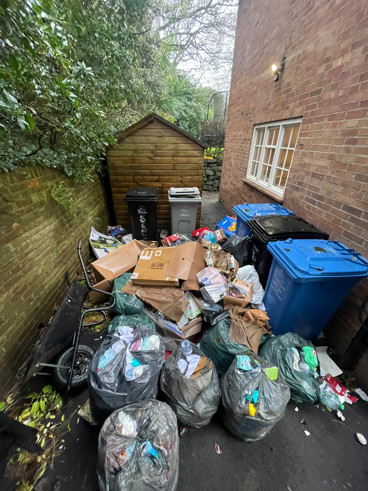 Bags of recycling, cardboard and wheelie bins crowding a narrow side passage