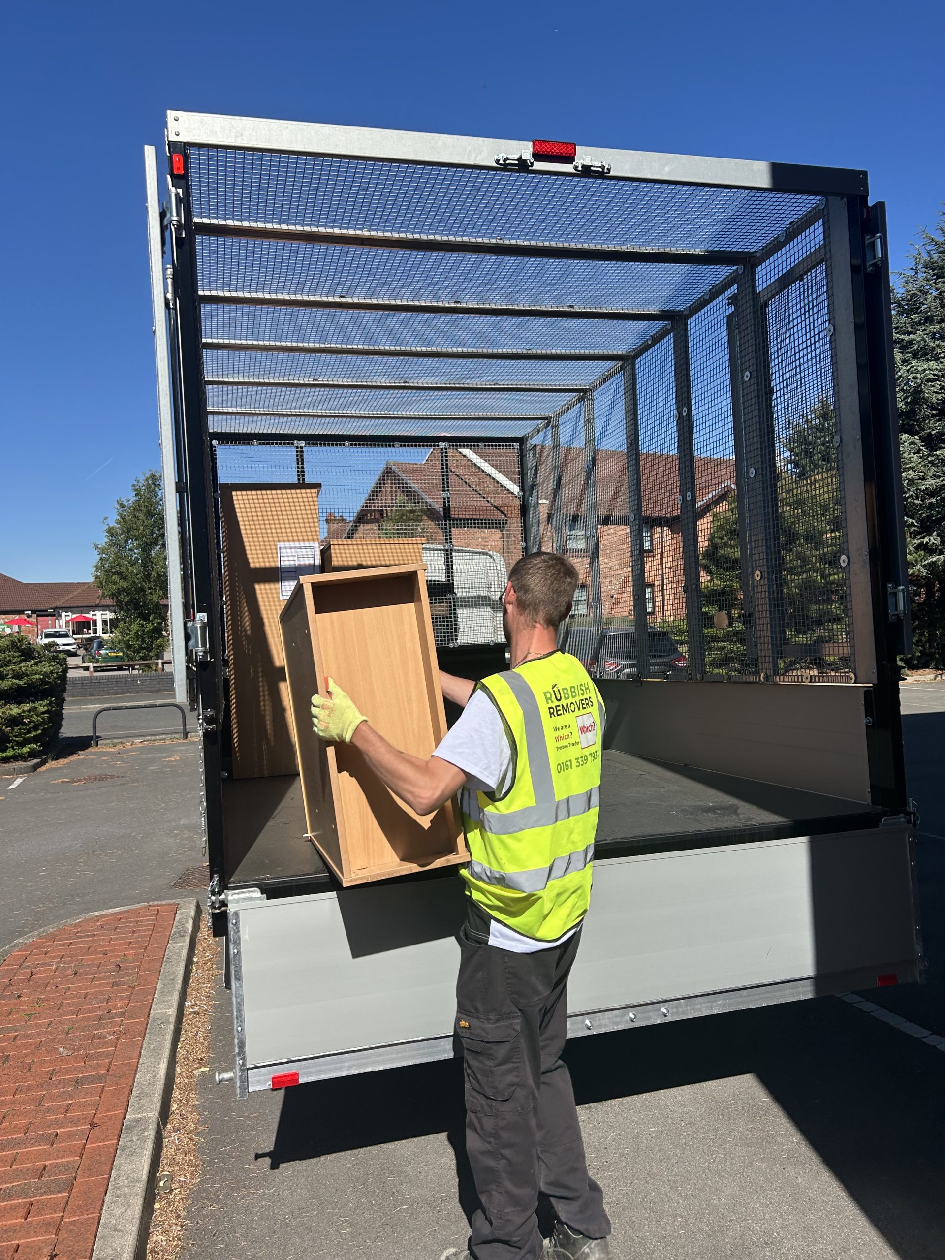 Worker in hi-vis loading a wooden cabinet into a caged tipper truck from its tail lift