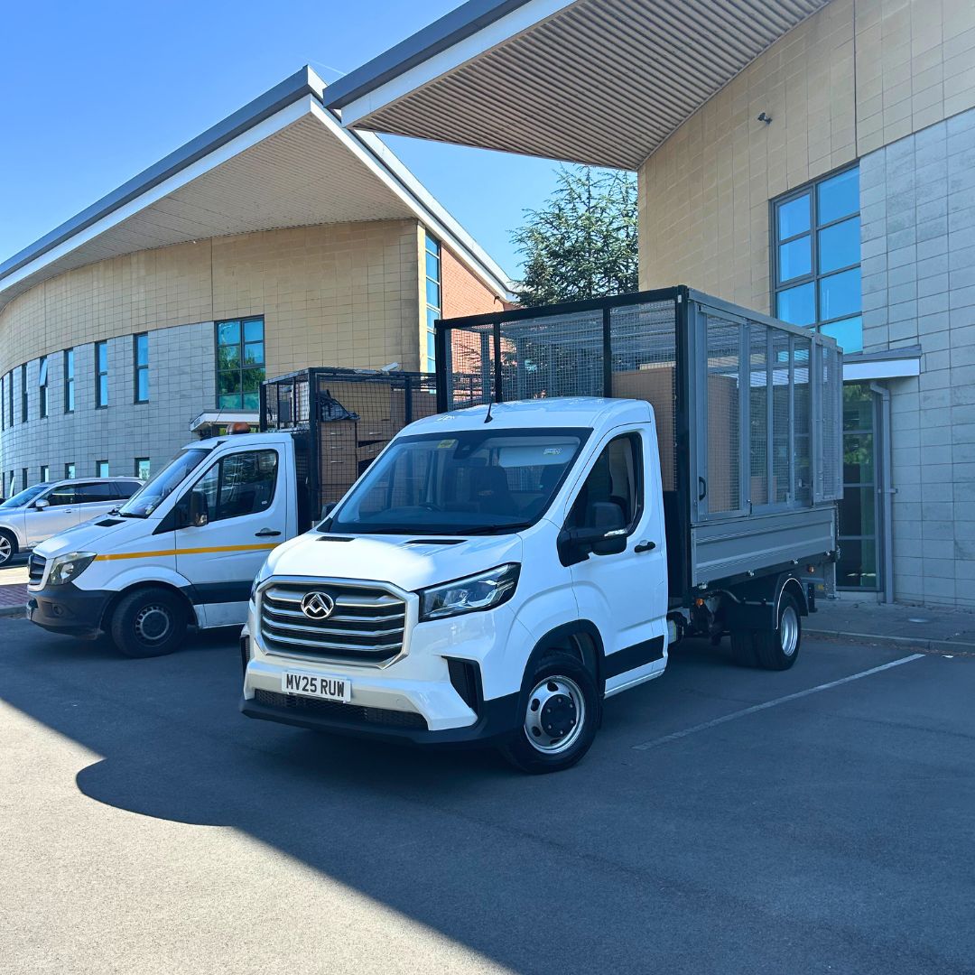 Two white caged tipper trucks parked outside a modern office building