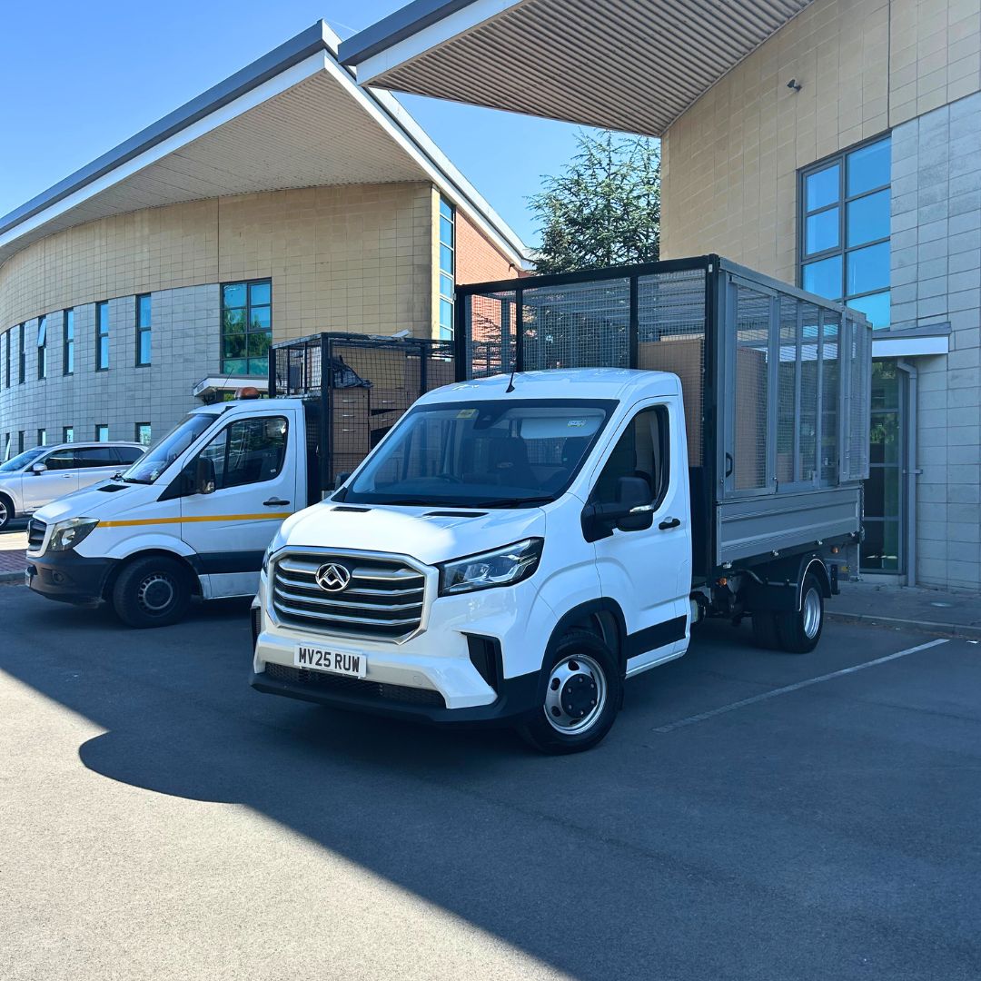Two white caged tipper trucks parked outside a modern office building