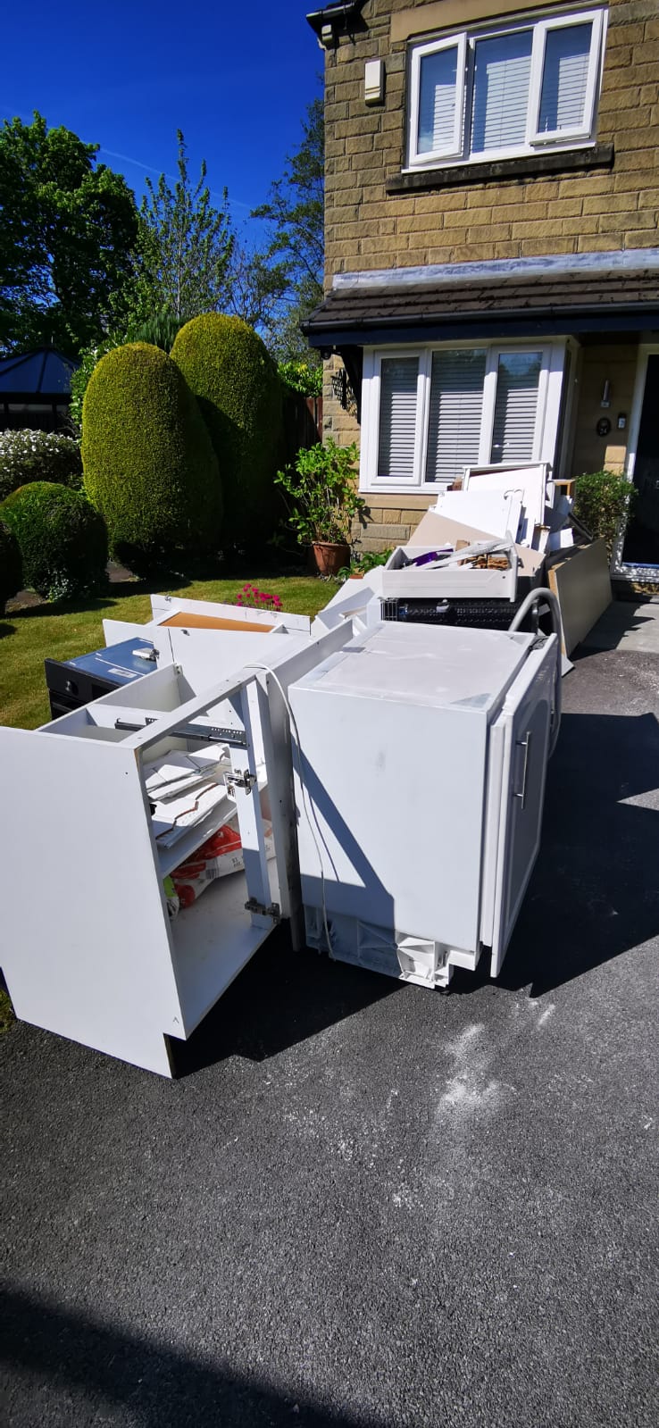 Old kitchen units and appliances left on a driveway outside a house