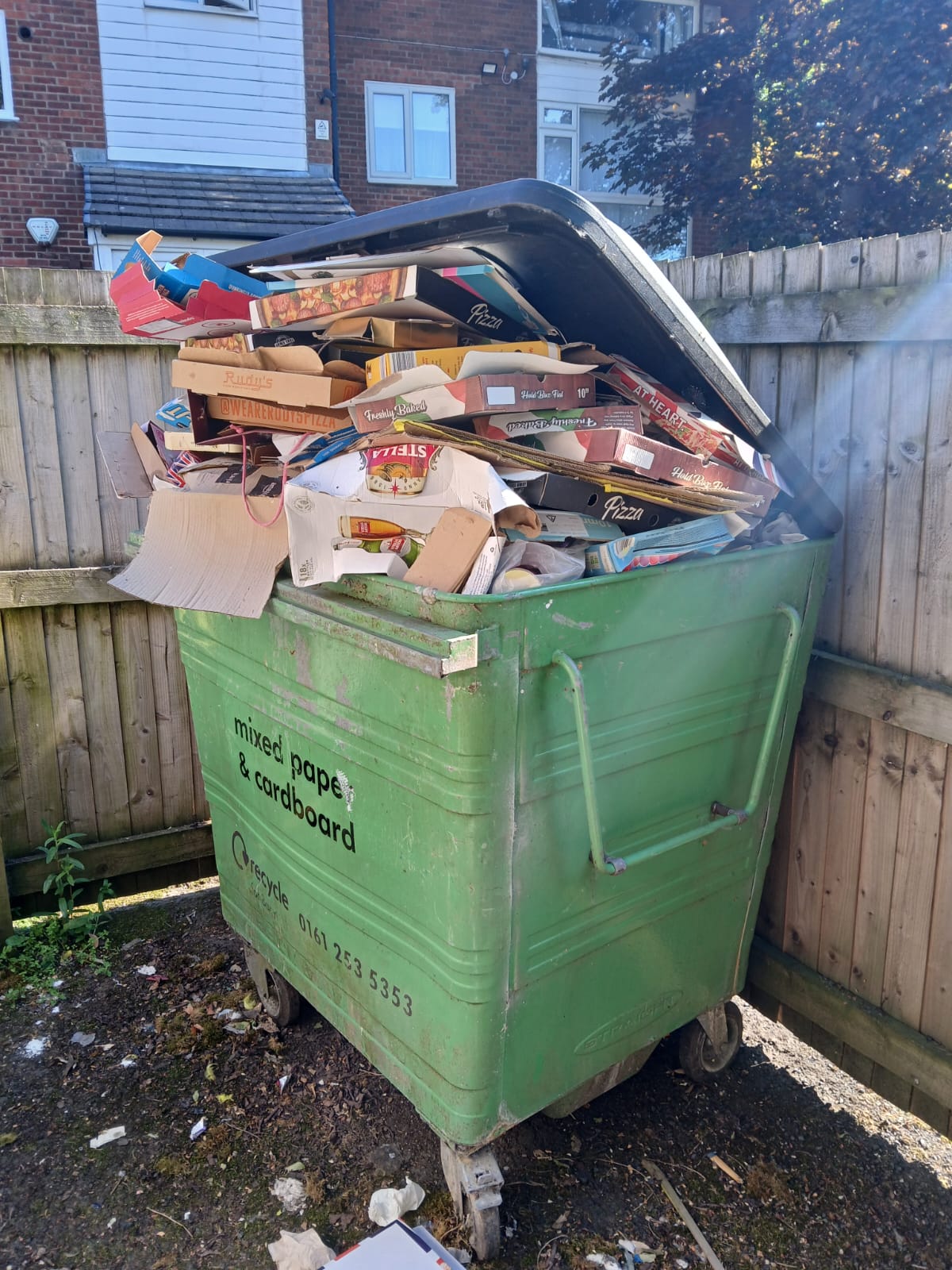 Overflowing green commercial bin piled high with cardboard and food packaging