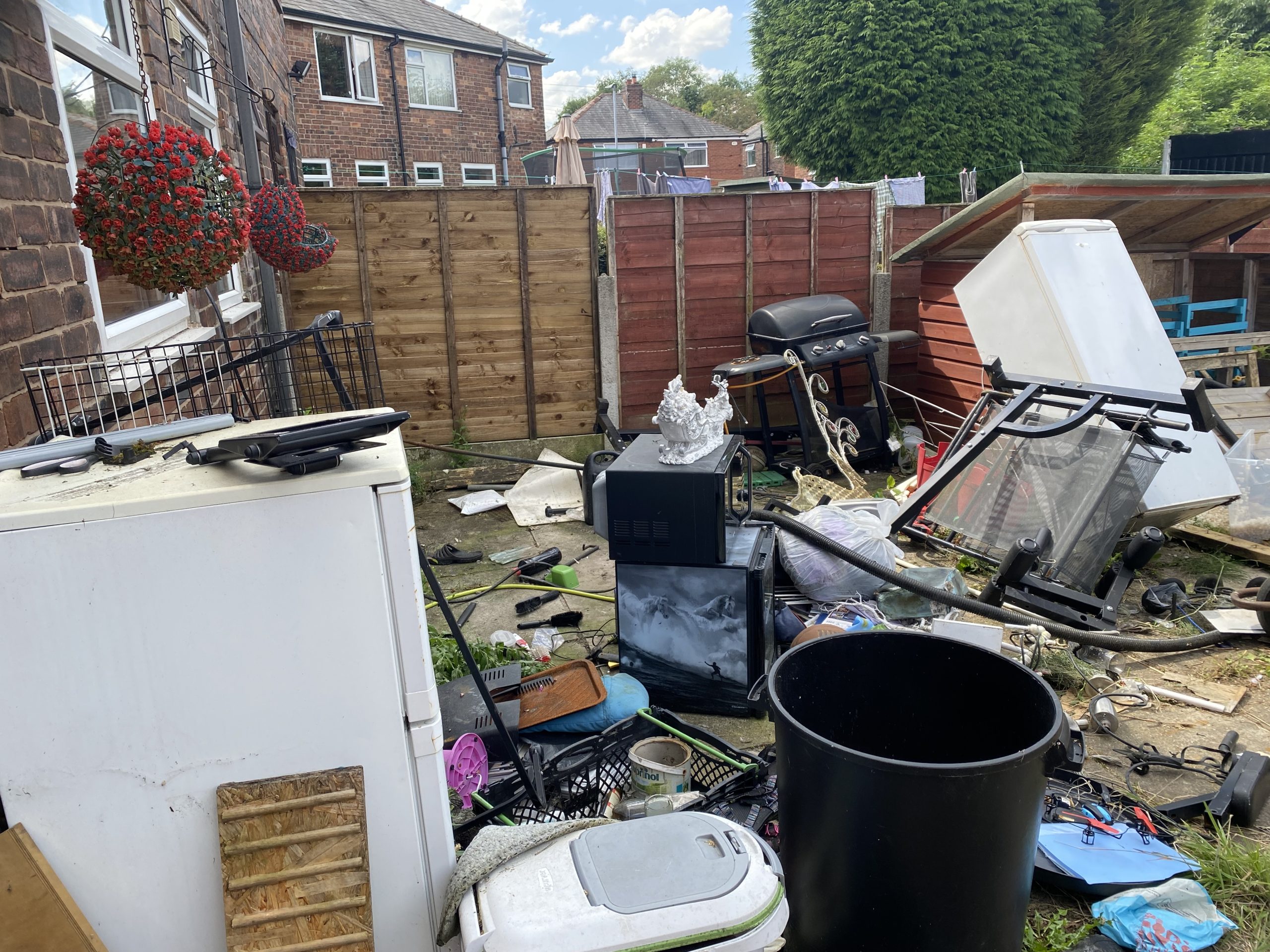 Back yard strewn with a fridge, garden furniture, bins and household junk
