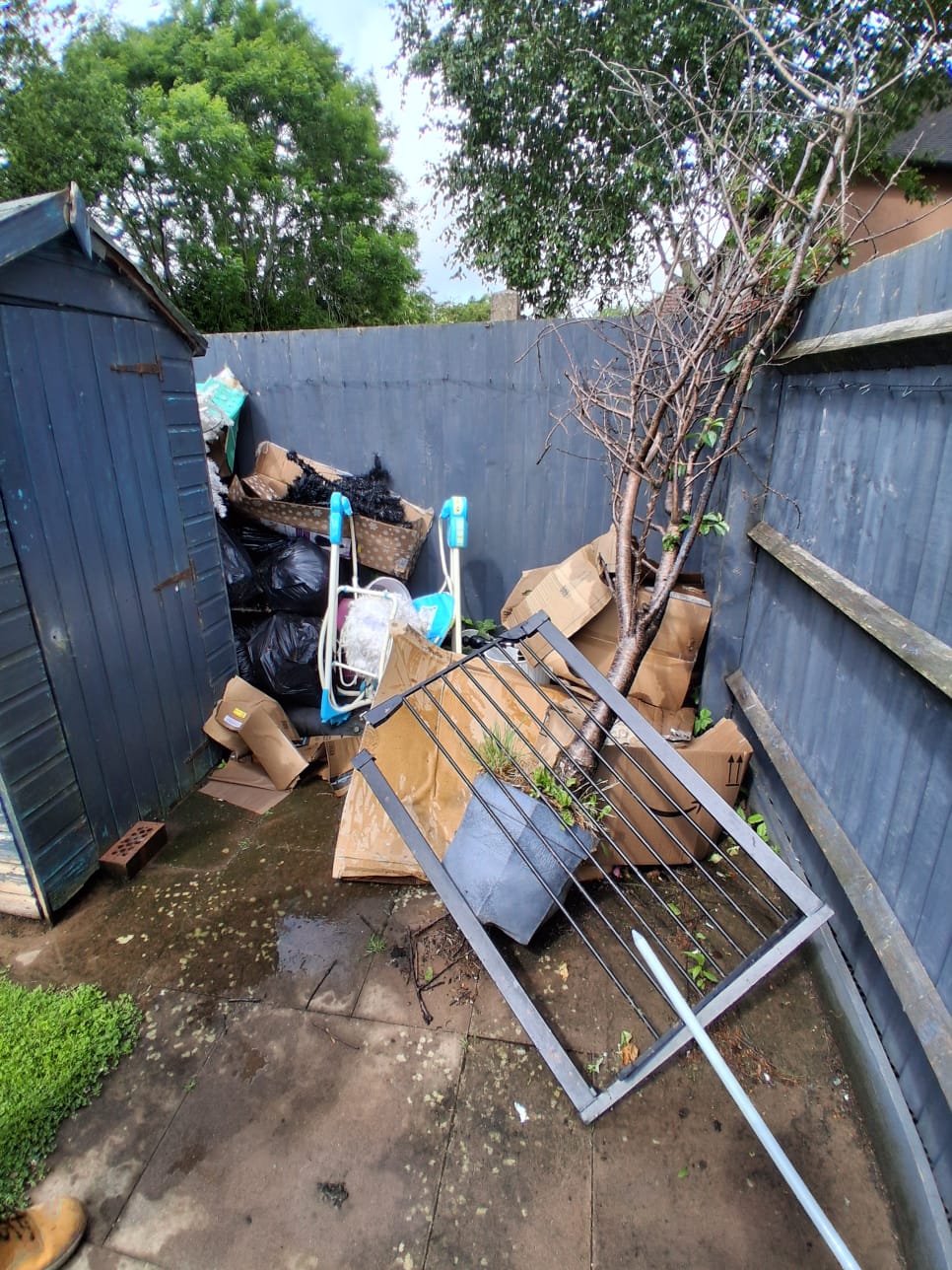 Broken garden furniture, boxes and household junk crammed into a narrow garden beside a shed
