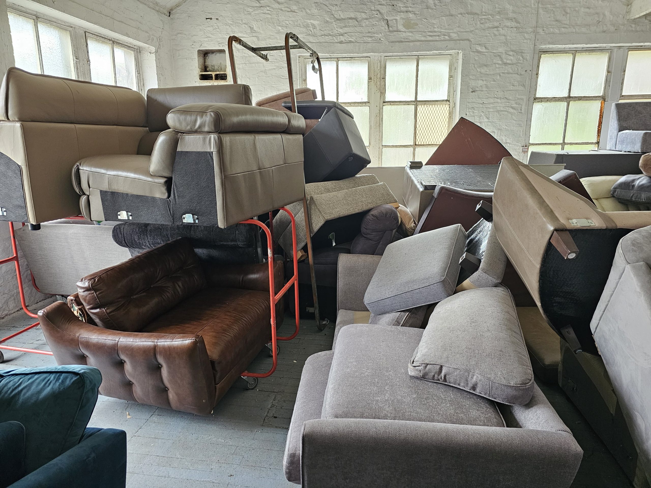 Sofas, armchairs and a leather settee piled high in a room awaiting clearance