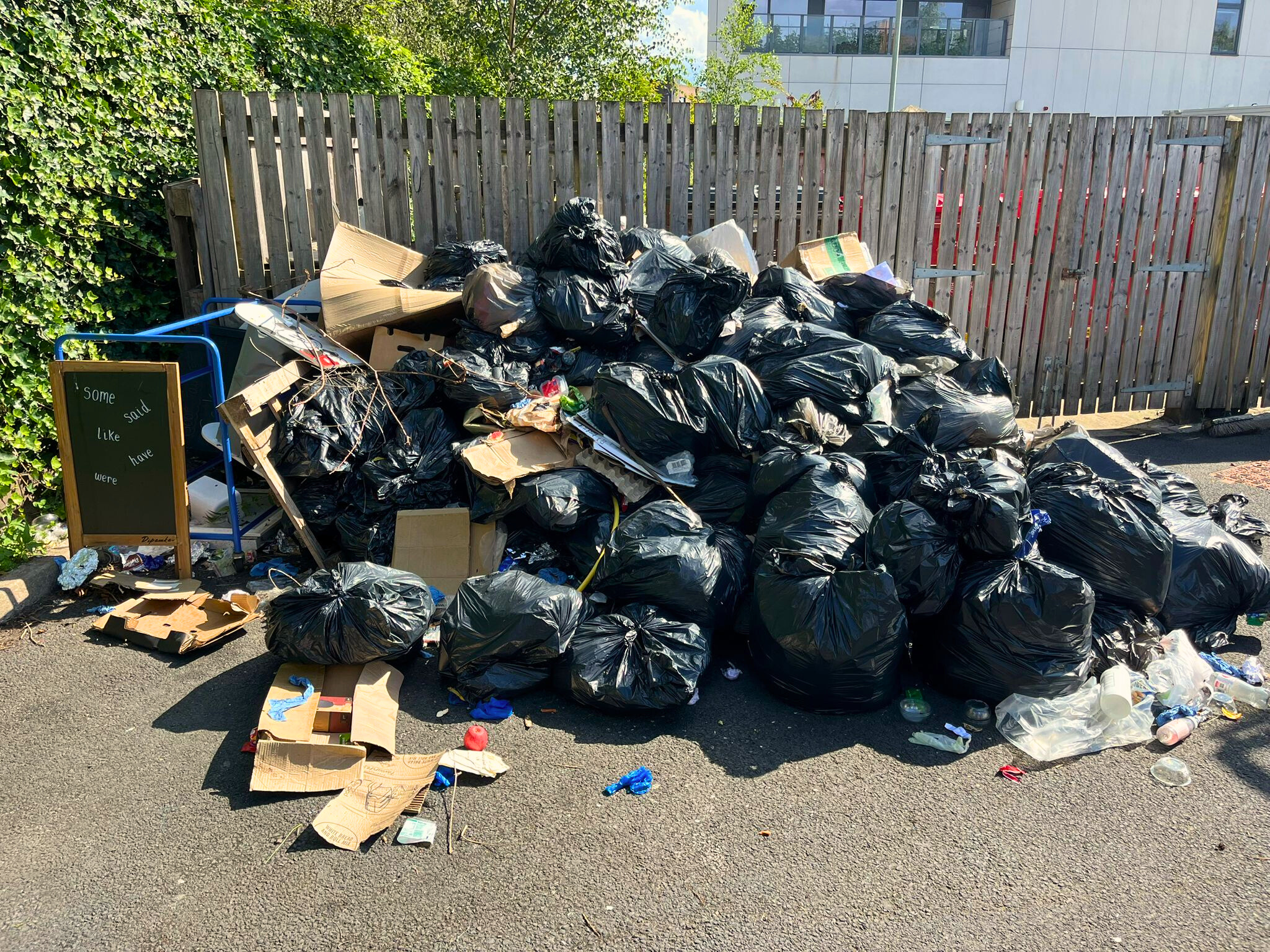 Large heap of black bin bags and flattened cardboard dumped against a fence