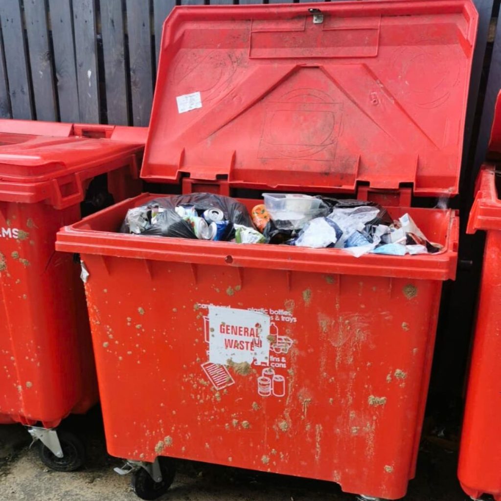 Overflowing red wheeled bin labelled General Waste