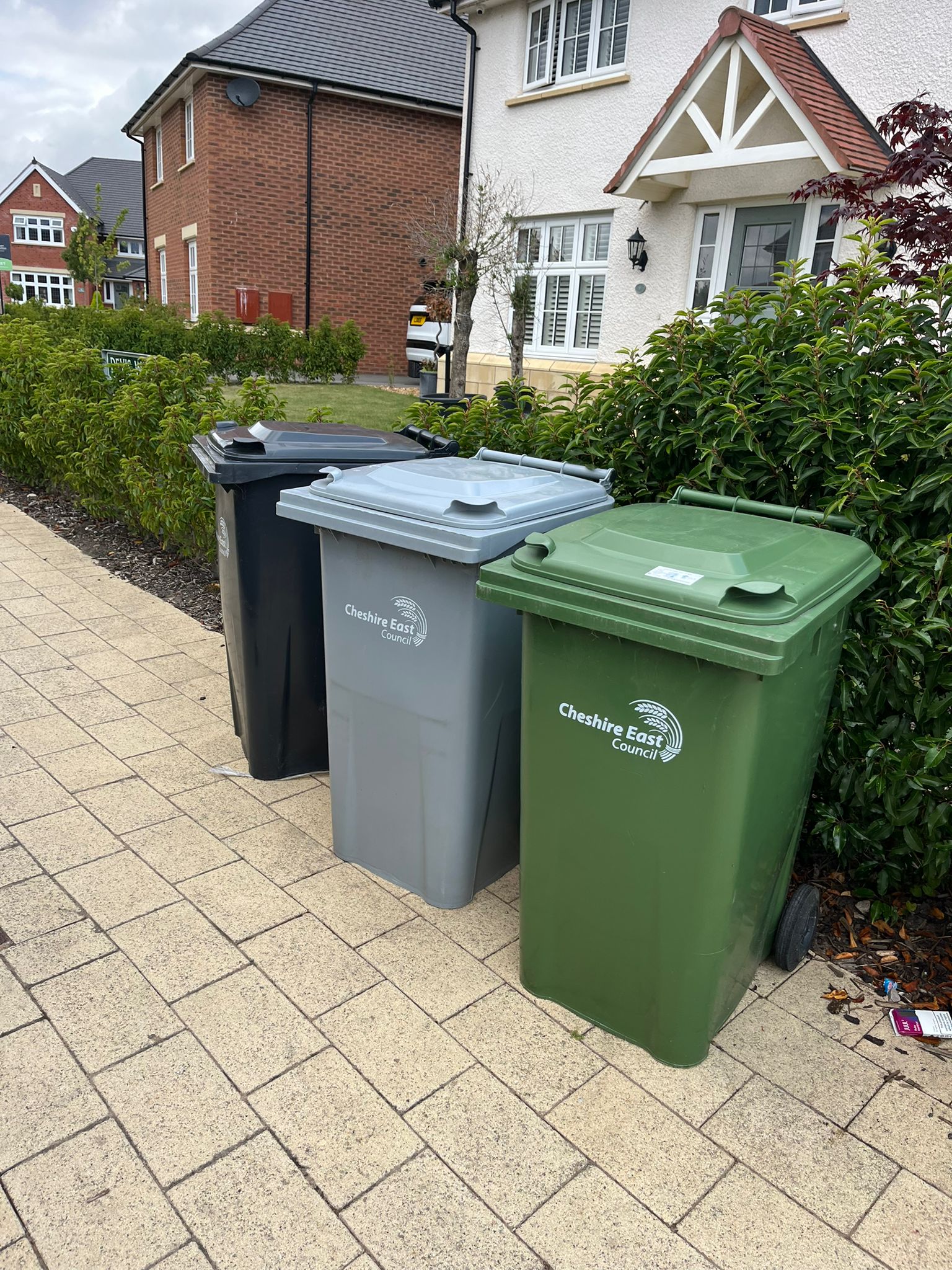 Black, grey and green household wheelie bins outside a new-build house