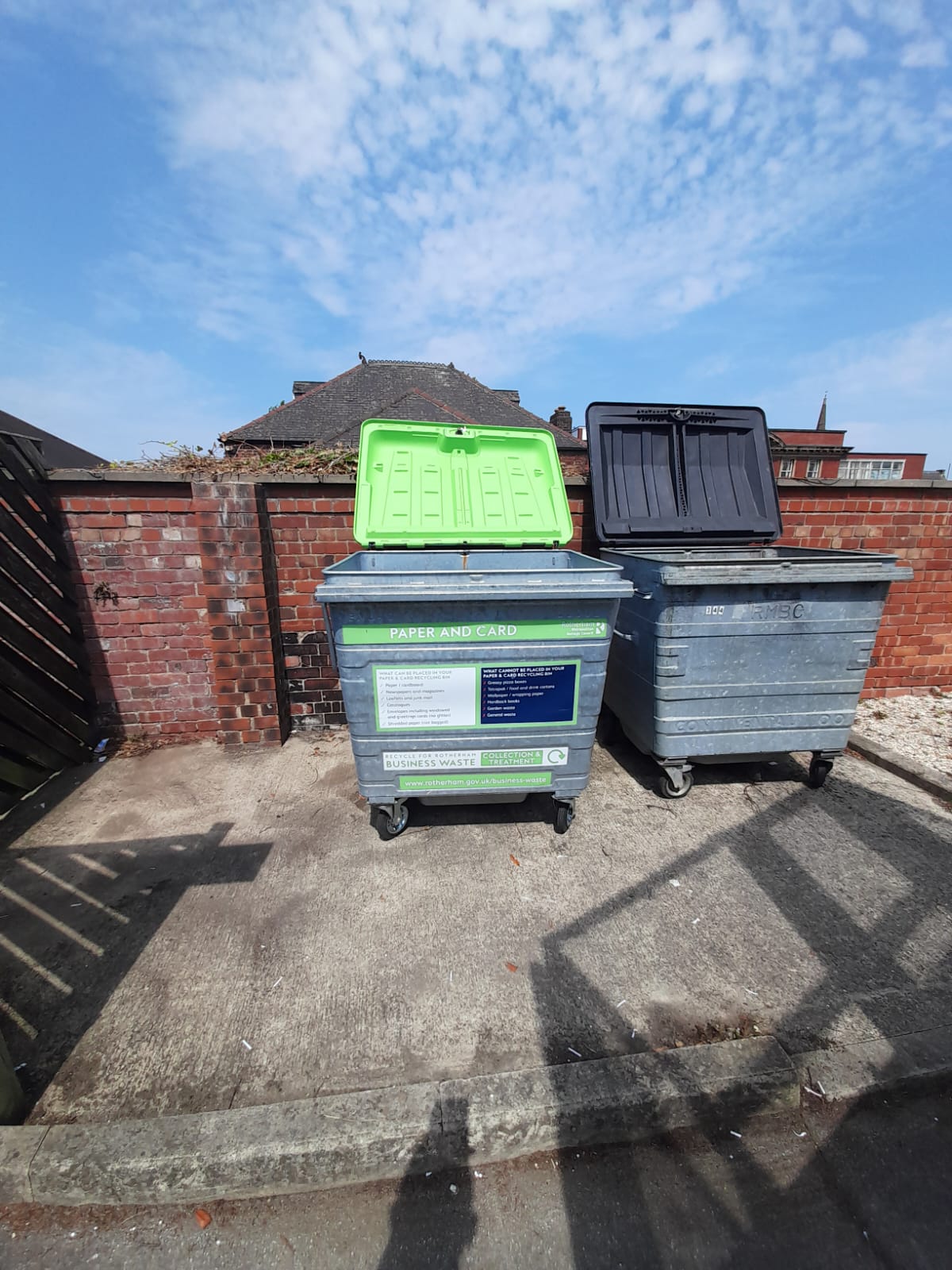 Two large wheeled commercial bins in a walled yard