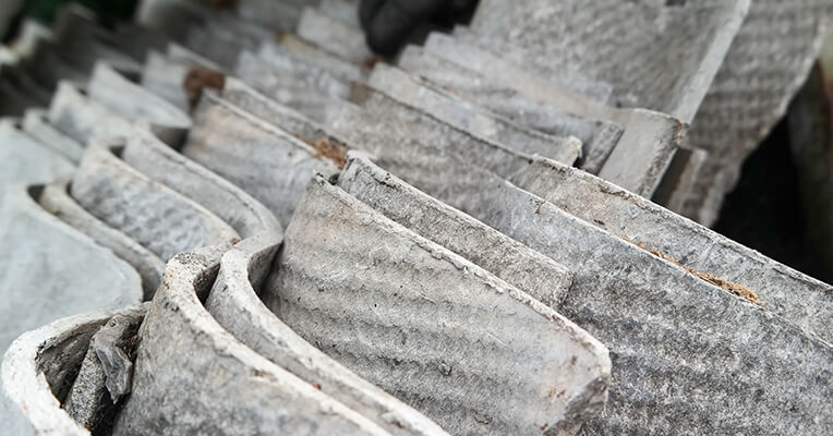 Close-up of broken, weathered corrugated cement roofing sheets stacked together