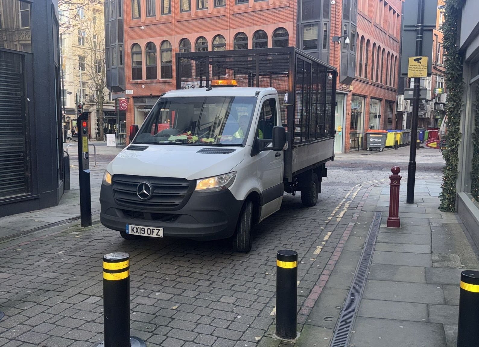 White Mercedes caged tipper truck parked on a cobbled city-centre street lined with bollards