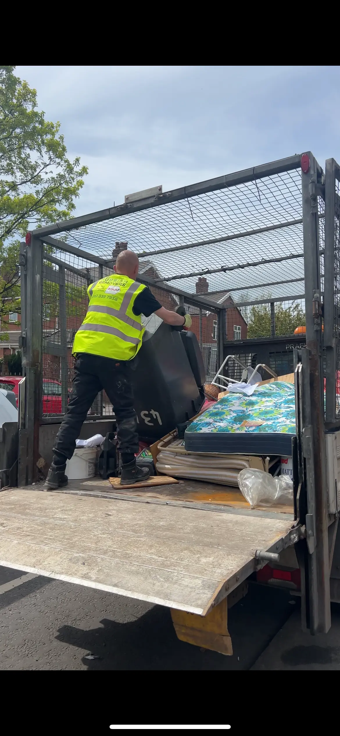 Worker in a Rubbish Removers hi-vis vest loading a wheelie bin into a caged tipper beside a mattress
