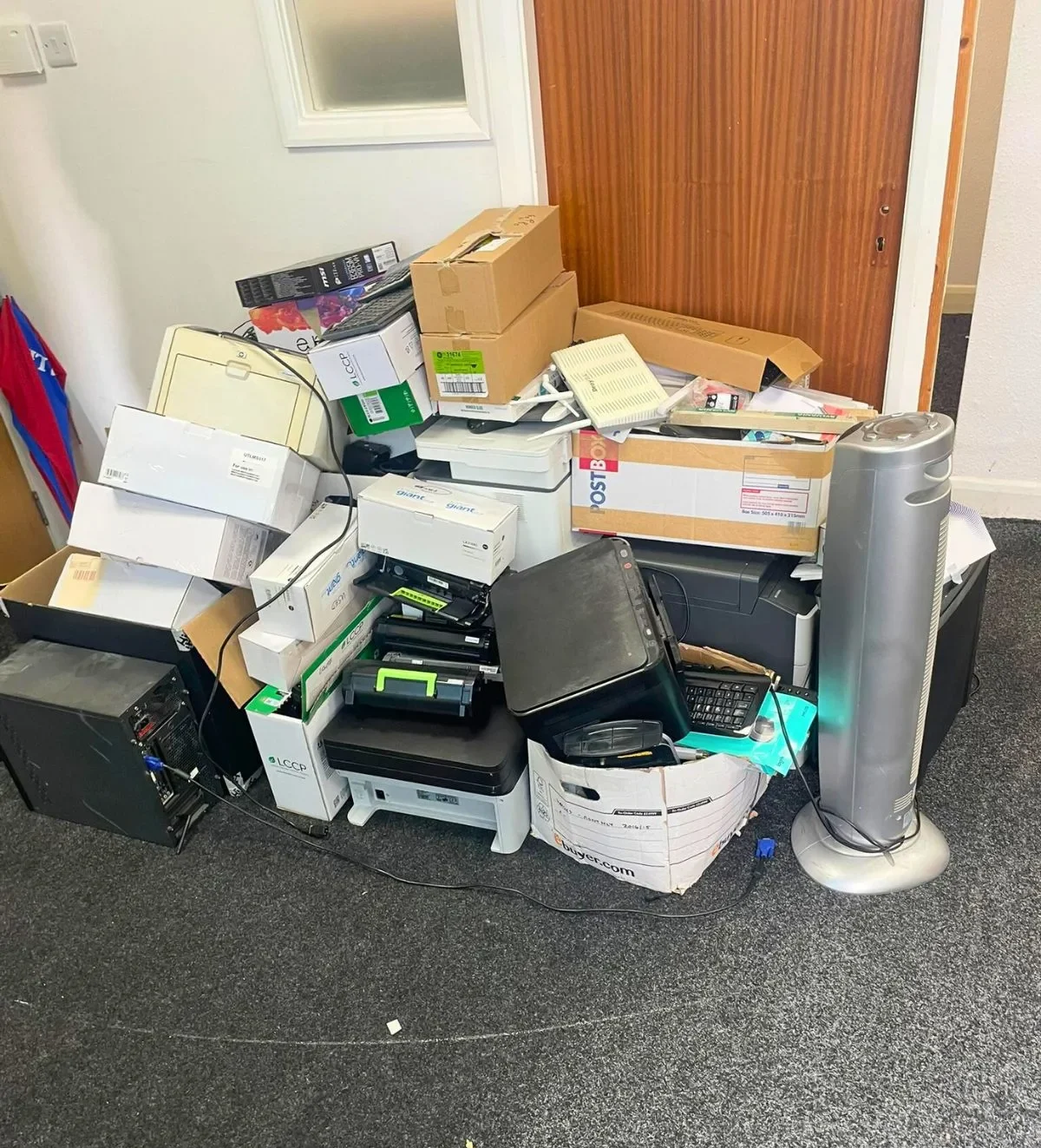 Printers, computers, cables and boxes of electrical waste piled in an office corner