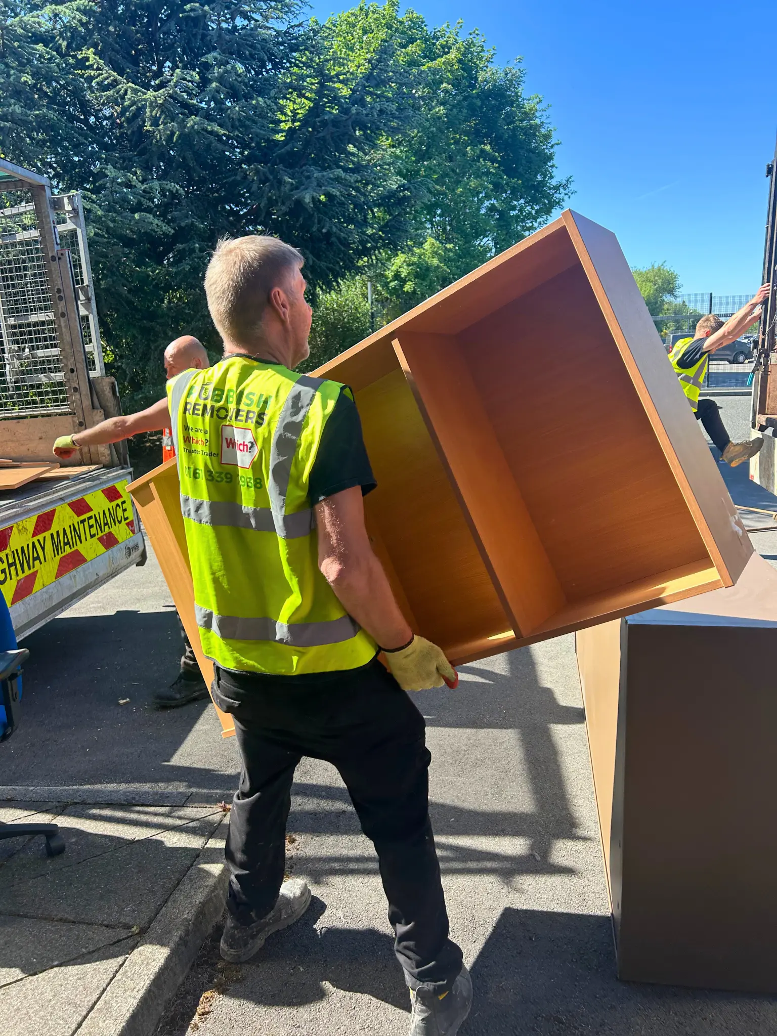 Worker in hi-vis carrying a wooden cabinet to a waste collection truck