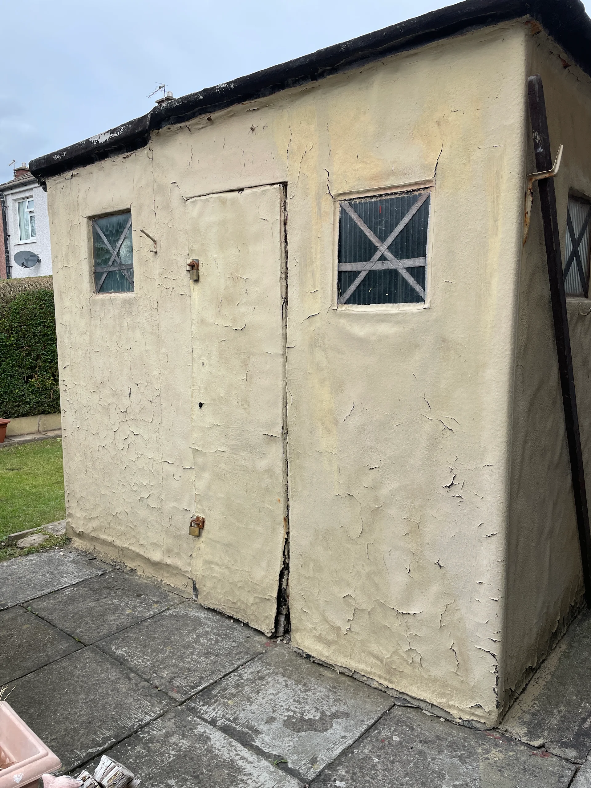 Weathered rendered shed with a door and two windows on a paved patio