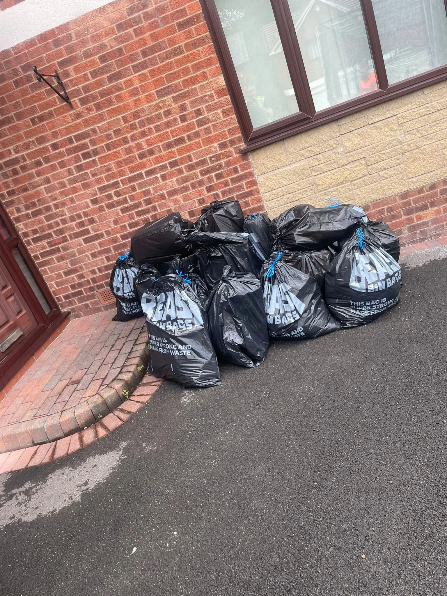 Pile of full black bin bags against a brick wall