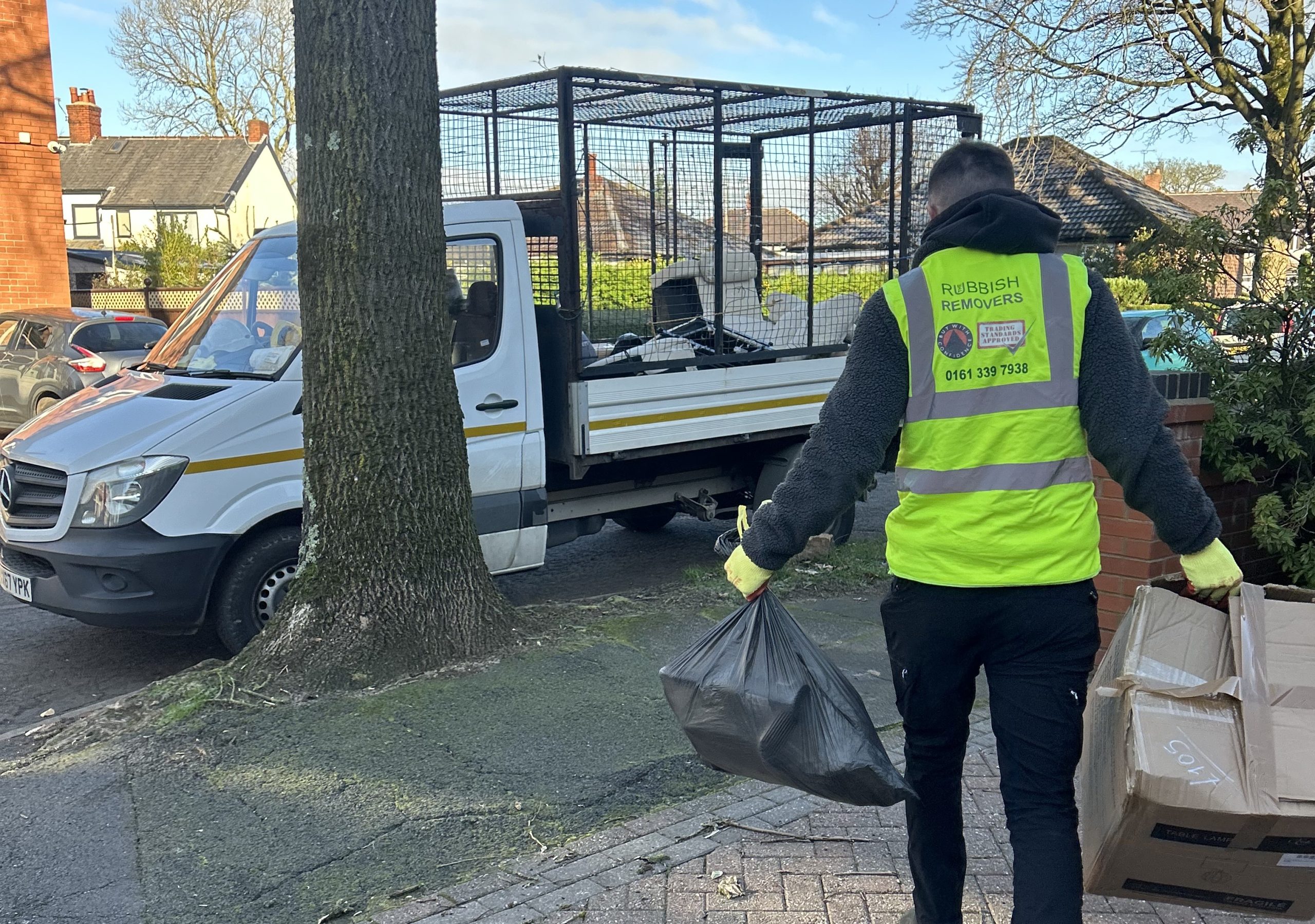 Worker in a Rubbish Removers hi-vis vest carrying a bin bag to a caged tipper truck