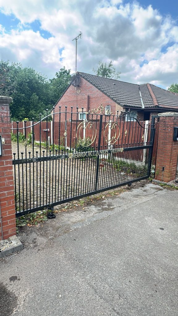 Driveway behind open black metal gates in front of a red-brick bungalow