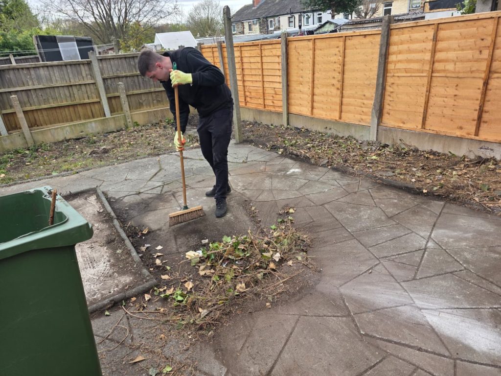 A trusted uniformed team member sweeping the remaining green waste from a customer garden